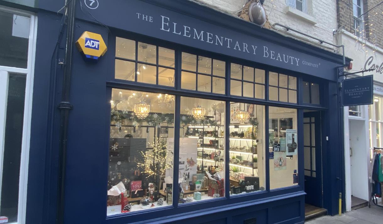 Outside The Elementary Beauty Company in Greenwich. An elegant navy blue shop front with windows that show a range of beauty products.