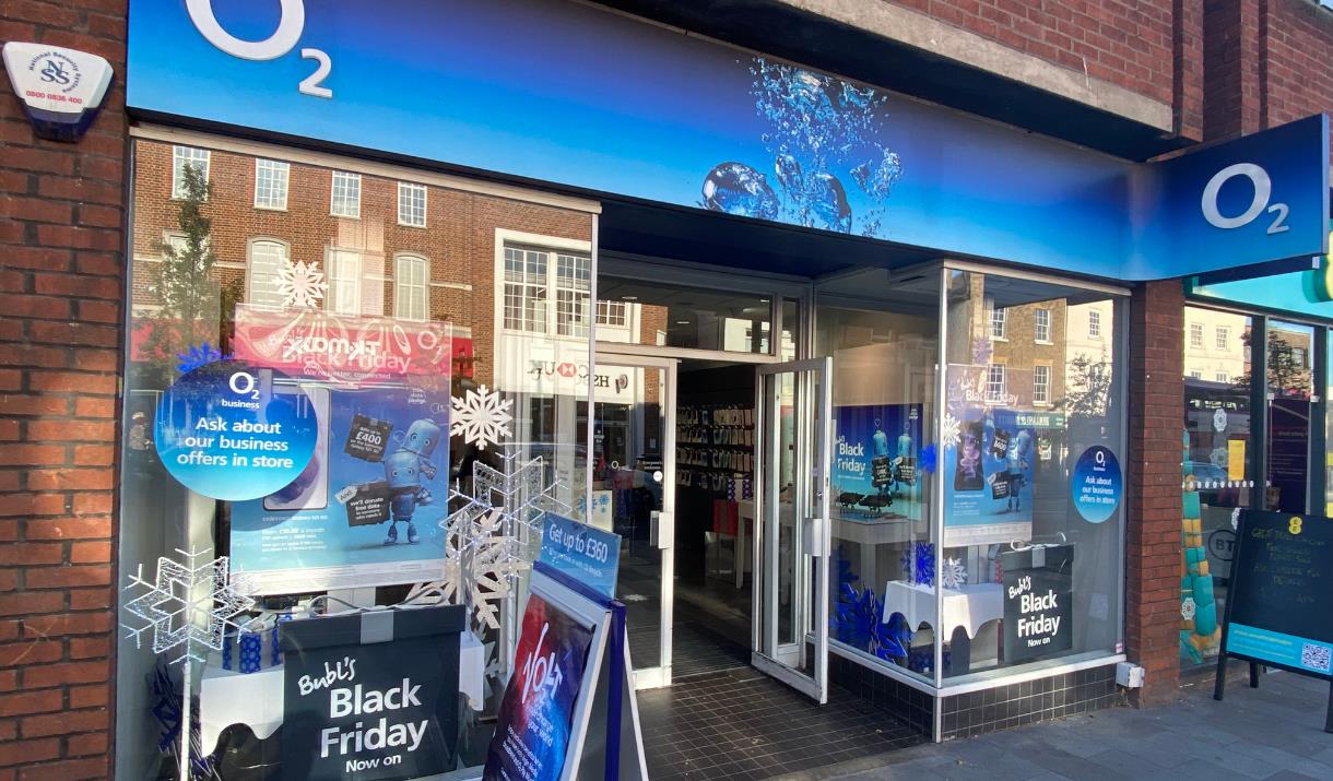 Outside O2 in Eltham. This picture shows a modern shop with lots of blue O2 advertising and windows looking onto a range of products.