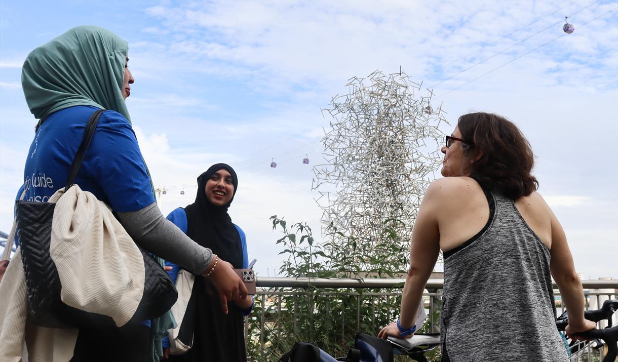 Two youth guides talking with a guided tour participant in front of Antony Gormley's 'Quantum Cloud' installation