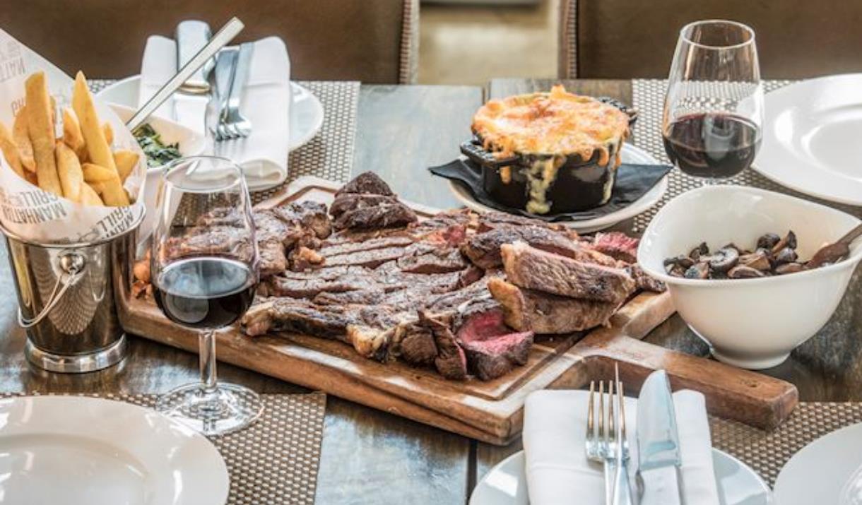 A delicious table of food including steak, chips and mac n cheese served to perfection at Manhattan Grill.