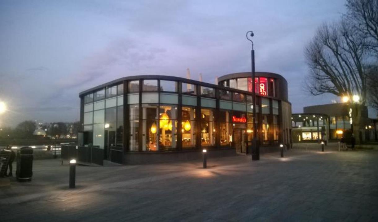 Outside Nando's next to The Cutty Sark in Greenwich, showing a modern building with lots of seating and a view onlooking the river Thames.