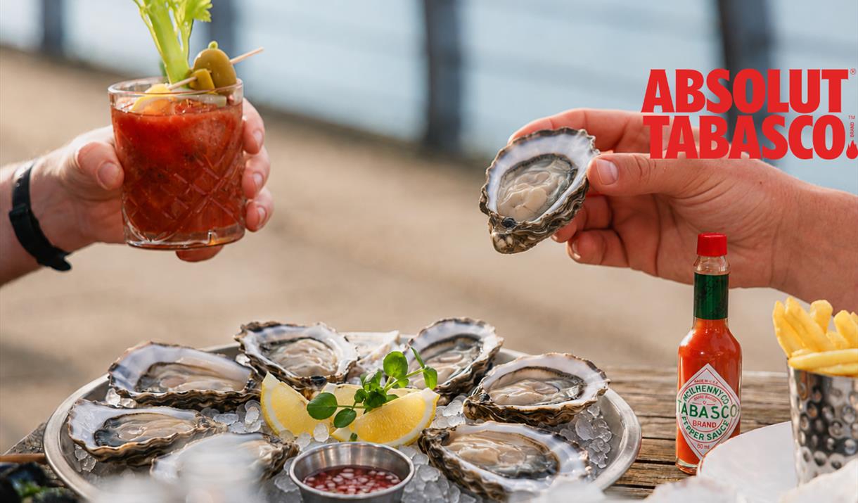 Friends enjoying oysters and Bloody Marys at a trendy Greenwich riverside spot overlooking the London skyline