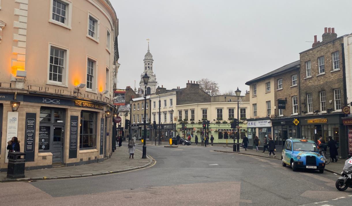 Greenwich High Street. A road filled with beautiful shops and restaurants. Also showing people walking down the pavement.