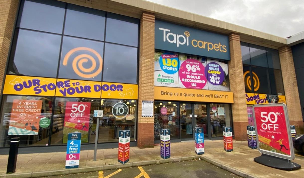 Tapi Carpets in Charlton. A large orange, white and navy building with automatic doors and large windows looking into the shop.