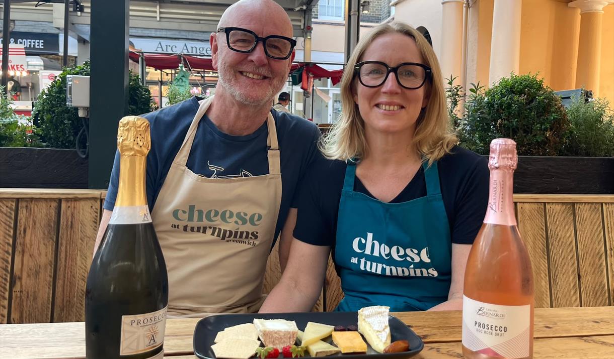 Cheese at Turnpins (cheese shop) owners sitting in the Admiral Hardy terrace in Greenwich Market with a cheese tasting platter and two bottles of Pros