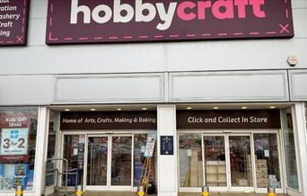 Outside Hobbycraft in Charlton. A large building with a purple and white banner. Through the windows you can see a large collection of products.