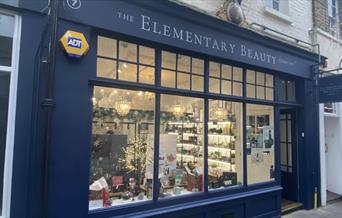 Outside The Elementary Beauty Company in Greenwich. An elegant navy blue shop front with windows that show a range of beauty products.