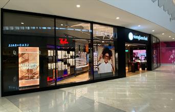 Outside Sunglass Hut at The O2. A glass shopfront looking into a huge selection of sunglasses.