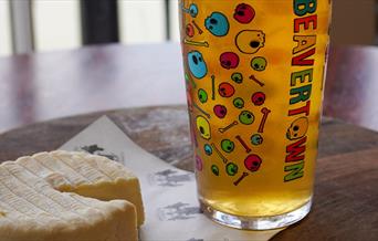 A glass of Beavertown beer and a round cheese.