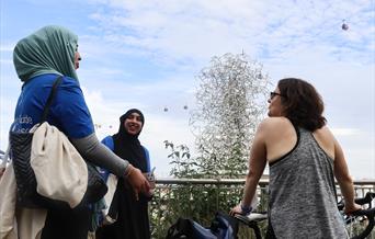 Two youth guides talking with a guided tour participant in front of Antony Gormley's 'Quantum Cloud' installation