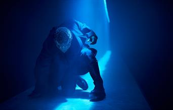 Live performance in action with neon blue light shining on a performer in the Troy World at The Burnt City