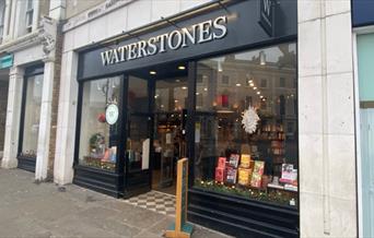 Outside Waterstones in Greenwich, showing a black shop front with a range of books through the window.