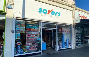 Outside Savers in Eltham. A white shop with a blue and red logo and a selection of products in the window.