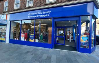 Outside Greenwich & Bexley Community Hospice in Eltham. A dark blue and white shopfront with a huge selection of items through the window.
