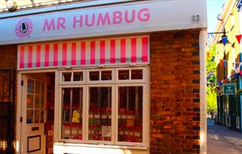 Outside Mr Humbug in Greenwich. A pink and white striped shop front with a mouth watering selection of sweets in the window.