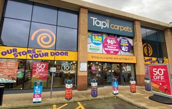 Tapi Carpets in Charlton. A large orange, white and navy building with automatic doors and large windows looking into the shop.