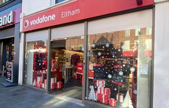 Outside Vodafone in Eltham. A modern red and white shop with Christmas decorations in the window.