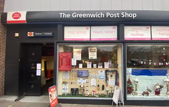 Outside Greenwich Post Office. A black, red and white shopfront with a window showing envelopes and other stationary.