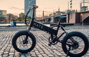 A picture of a black and white mate bike, set next to a river and infront of a stunning sunset.