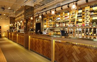 All-Bar-One bar image with well lit up counter with a range of beer taps and a wide selection of wine bottles on the shelves behind.