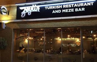 Exterior image of Zeytin Restaurant with glass entrance and warm lighting.