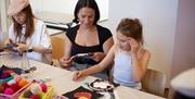A young girl and a woman sitting at a table using embroidery kits