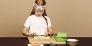A child rolling sushi with some ingredients set up in front of her