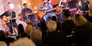 4 singer songwriters on stage, looking over the heads of an attentive audience. The heads of the audience in focus, the 4 artists on the stage