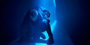 Live performance in action with neon blue light shining on a performer in the Troy World at The Burnt City