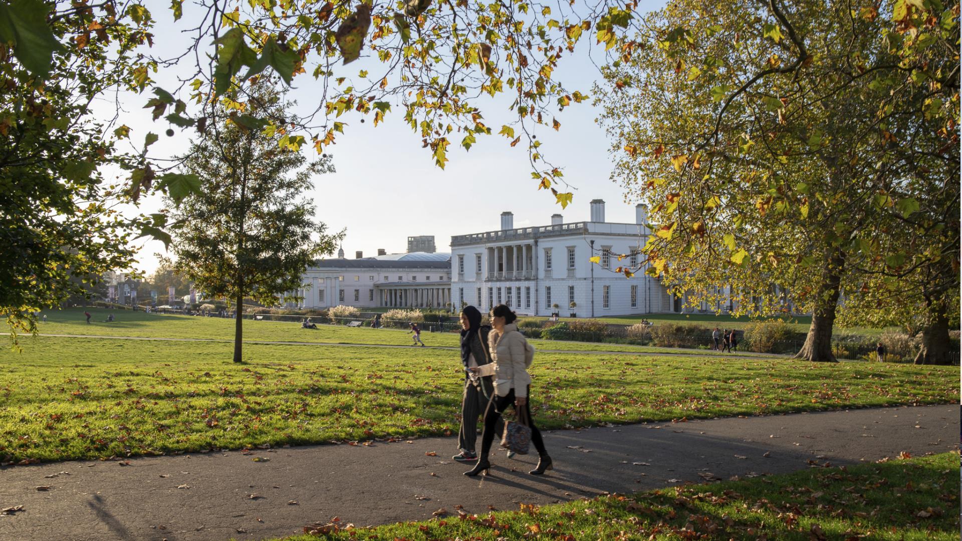 Two women walk through Greenwich Park in front of the Queen's House.