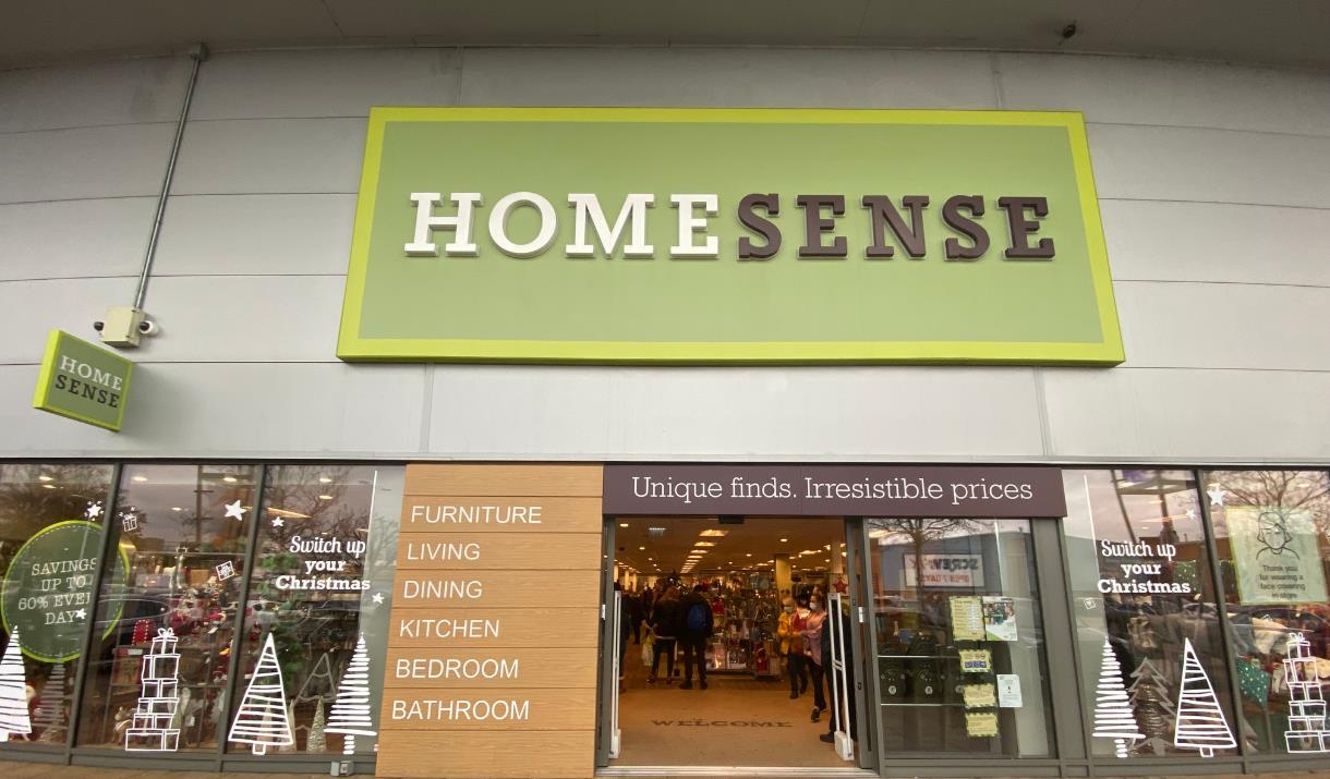 Outside Homesense in Charlton. A large silver building with a green, white and black sign at the top. There is also a row of windows showing all of th