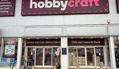 Outside Hobbycraft in Charlton. A large building with a purple and white banner. Through the windows you can see a large collection of products.