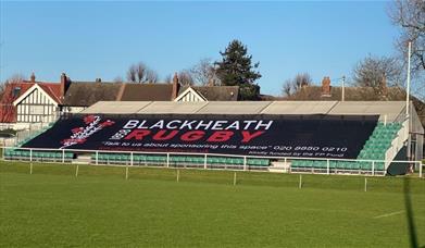 Blackheath Rugby Club ground with green seating in the background and black banner with the stadium name over the seating.
