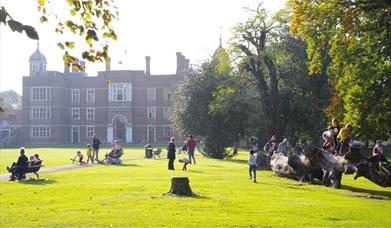 Kids playing beside Charlton House in Charlton Park and Parents relaxing on benches on a beautiful Sunny Day
