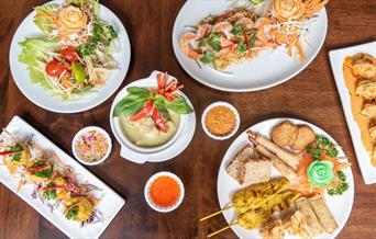 Table set with Kathi Thai Kitchen specialities including appetisers platter, papaya salad, green curry and more.