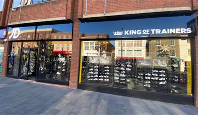 Outside JD Sports Eltham, showing a metallic black shop front presenting a wide range of products.
