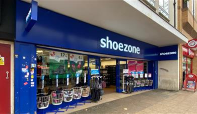 Outside Shoezone in Woolwich. A blue and white shop with shoes on display both inside and outside.