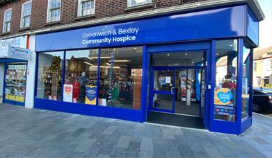 Outside Greenwich & Bexley Community Hospice in Eltham. A dark blue and white shopfront with a huge selection of items through the window.