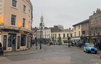 Greenwich High Street. A road filled with beautiful shops and restaurants. Also showing people walking down the pavement.