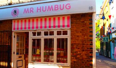 Outside Mr Humbug in Greenwich. A pink and white striped shop front with a mouth watering selection of sweets in the window.