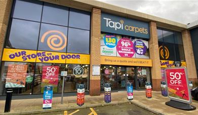 Tapi Carpets in Charlton. A large orange, white and navy building with automatic doors and large windows looking into the shop.