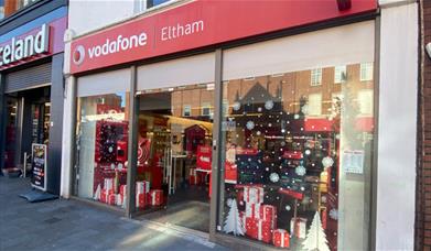 Outside Vodafone in Eltham. A modern red and white shop with Christmas decorations in the window.