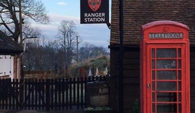 The Castle Park Ranger Station, with its sign containing the colchester coat of arms, with a red telephone box outside