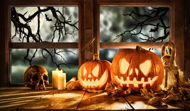 Carved pumpkins, candles and skull on windowsill