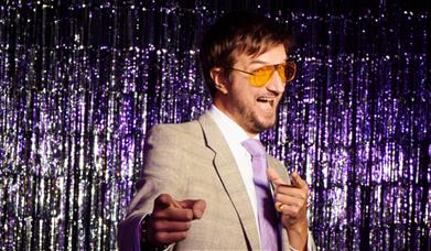 Man in yellow glasses with a purple glitter backdrop