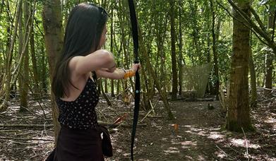 Woman with long hair shooting a recurve bow at a 3D target in a sunny woodland