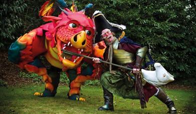 A comically dressed pirate  brushed the teeth of an oversized friendly dragon with a customised hobby horse