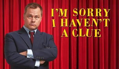 Jack Dee poses, arms folded in front of a Red Curtain and the text "I'm Sorry, I Haven't A Clue"