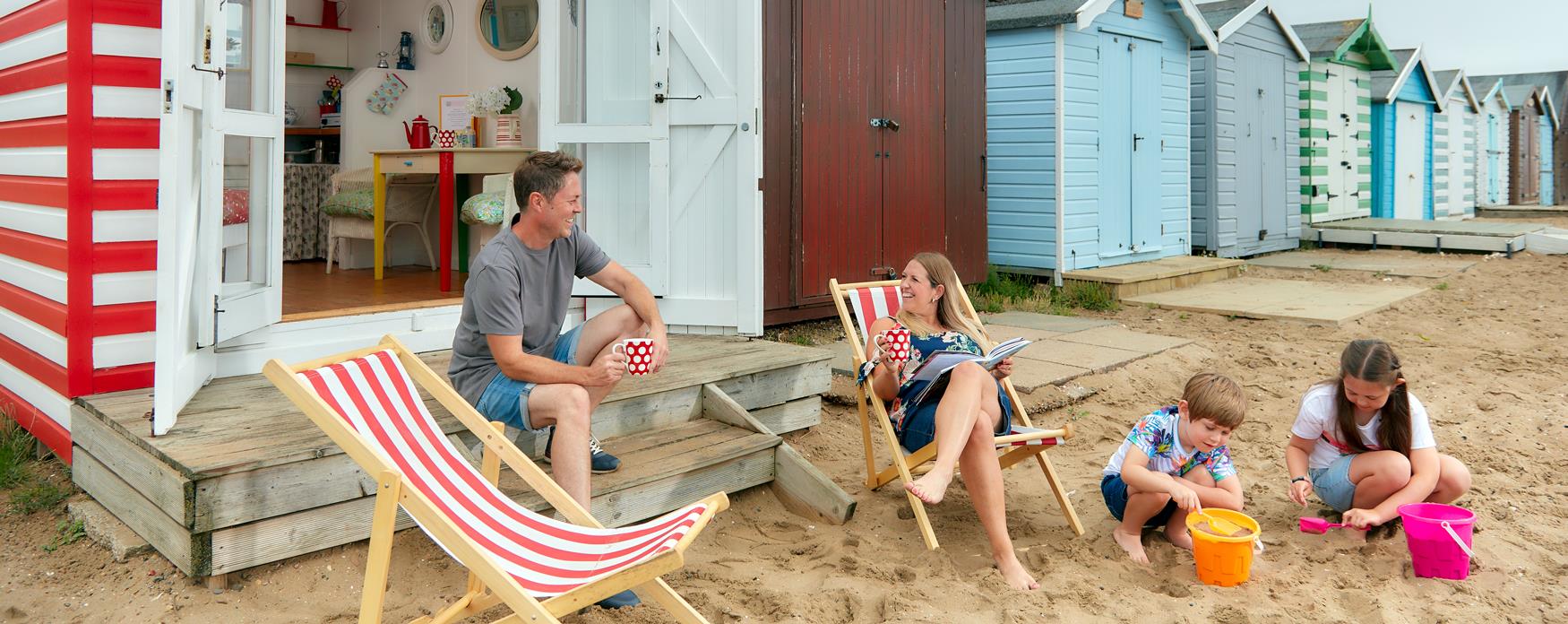 Family sitting outside red beach hut at Mersea island