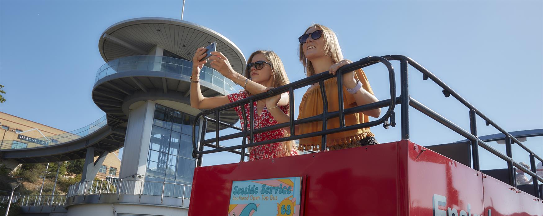 Two people on red  open top bus taking photo